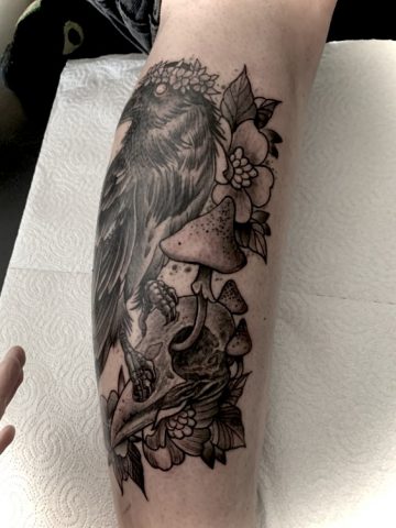 Schienbein Tattoo mit Rabe, Totenschädel und Pilzen im Traditional Blackwork Stil, detailreiches Custom Tattoo mit dunkler Symbolik, gestochen bei Talisman Tattoo – Sabine Jacobs in Raeren, Belgien, nahe Aachen, Eupen, Sankt Vith und Luxemburg