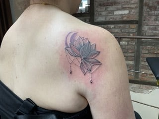 Lotusblüten Cover-Up Tattoo mit geometrischen Elementen auf dem Schulterblatt zum Überdecken einer kleinen Rose.