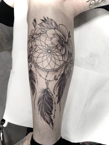 Dreamcatcher Tattoo im Fineline Stil mit Blumen, Federn und geometrischem Netz, detailreiches Linework Tattoo an der Wade außen, elegantes Black & Grey Tattoo mit feinen Schattierungen, gestochen bei Talisman Tattoo – Sabine Jacobs, exklusives Tattoo Studio in Raeren, Belgien nahe Aachen, NRW, Eupen, Sankt Vith, Luxemburg, Europa, internationale Tattoo Kundschaft