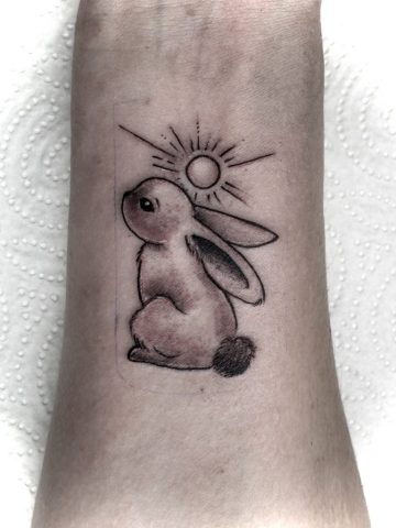 Hasen Tattoo im Fineline Stil mit Sonne und weichen Schattierungen, niedliches Tier Tattoo am Unterarm, minimalistisches Black & Grey Tattoo mit zarter Illustration, gestochen bei Talisman Tattoo – Sabine Jacobs, exklusives Tattoo Studio in Raeren, Belgien nahe Aachen, NRW, Eupen, Sankt Vith, Luxemburg, Europa, internationale Tattoo Kundschaft