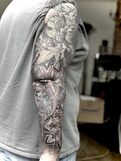 Japanischer Black-and-Grey Sleeve mit großer Chrysantheme, Lotusblüte, geometrischen Mustern und ornamentalem Hintergrund am gesamten Arm.
