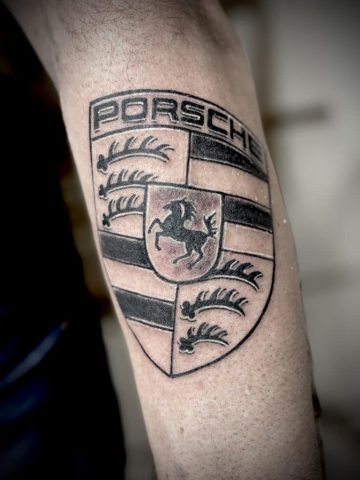 Realistisches Porsche Wappen Tattoo in Black & Grey auf dem Unterarm. Präzise gestochenes Automobil-Logo mit feinen Linien, satten Schwarztönen und originalgetreuen Details.