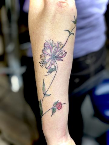 Farbiges Blumenranken Tattoo mit zarten Blüten und feinen Linien als florales Arm Tattoo.