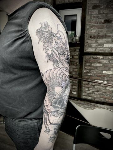 Japanischer Tattoo Sleeve mit Drachenkopf, Koi Karpfen und Pfingstrosen in Black & Grey auf dem Ober- und Unterarm. Detailreiche asiatische Tätowierung im Irezumi-Stil mit feinen Schattierungen und traditionellen Elementen.